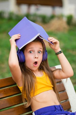 Preteen school girl with book on bench in park