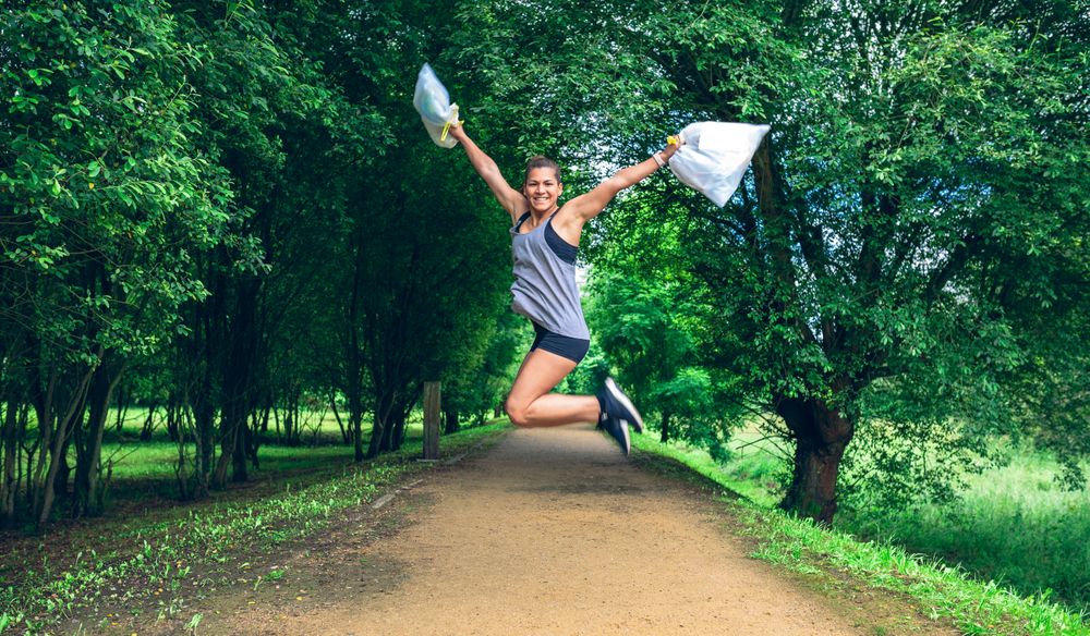 Woman jumping with trash bags after volunteering to clean up park