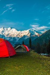 Red tents camping facing snow capped mountains in Pakistan, vertical composition