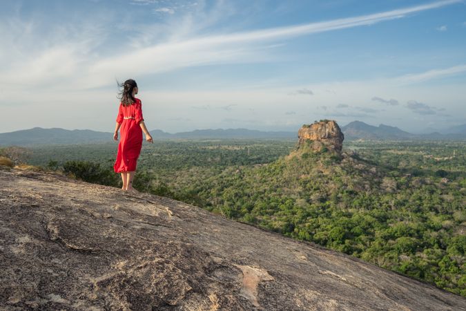 Tourist against solitary rock in middle of green forested plain under clear sky in summer