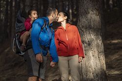 A couple kissing while hiking with their daughter in a child carrier.
