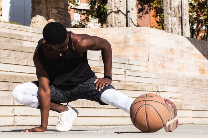 Black sportsman stretching on basketball court