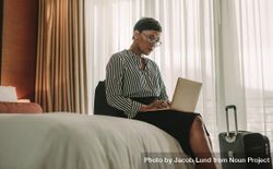 Businesswoman sitting on bed using laptop 0g7j80