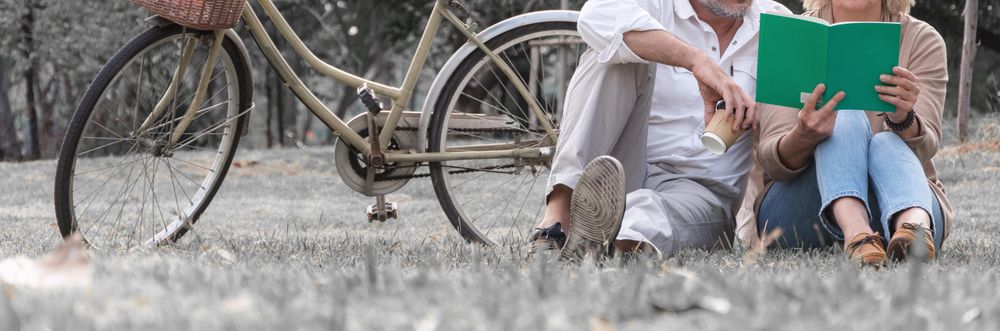 Older male and female sitting in the grass in public park with bicycle