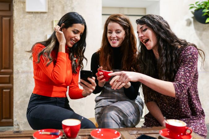Friend showing phone screen to her friends in coffee shop