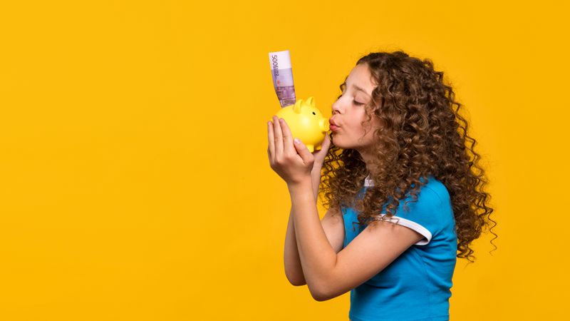 Girl kissing piggy bank, showing appreciation for saving money.