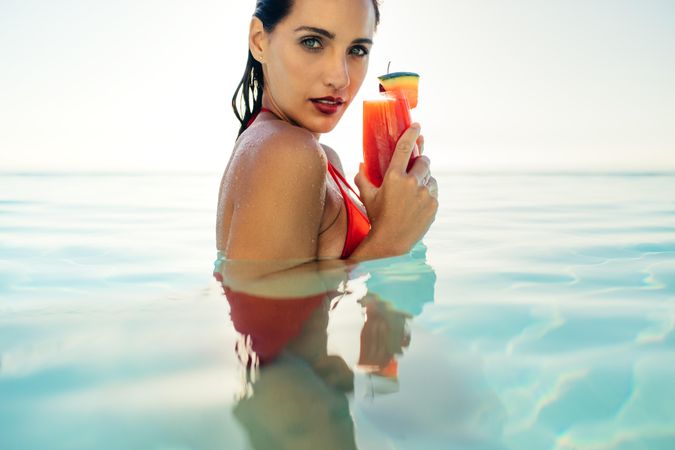 Young woman holding a cocktail while standing in an infinity pool