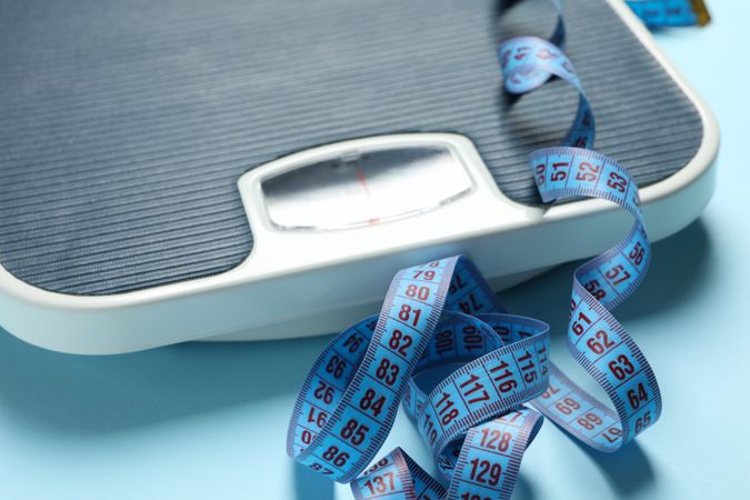 Scales and measuring tape on blue background. Weight loss concept