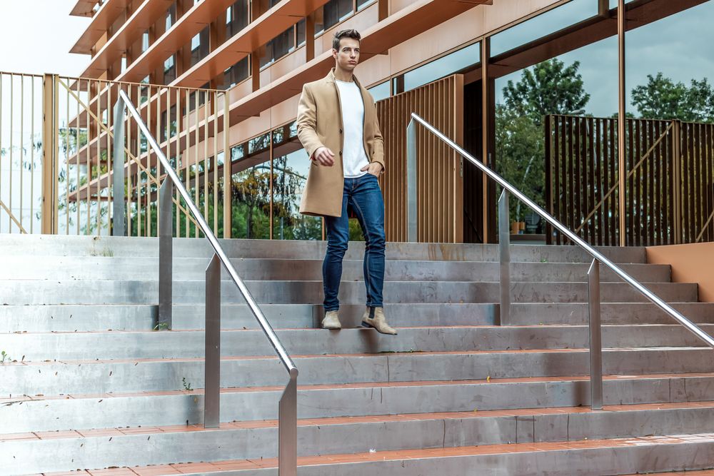 Man in camel coat walking down staircase outside