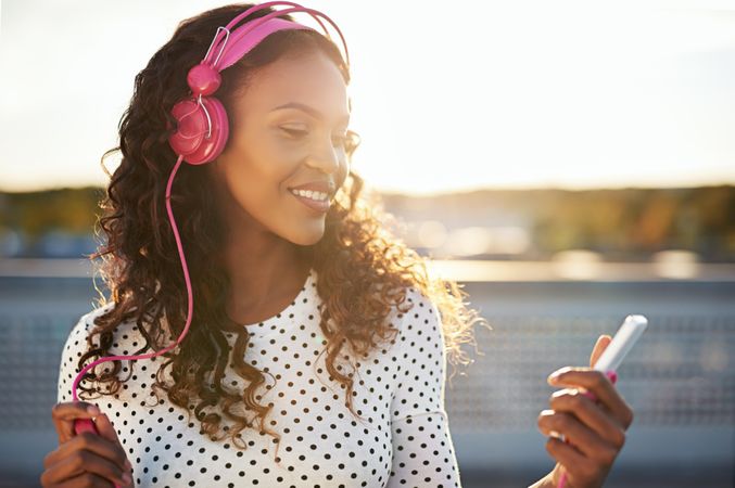 Attractive Black woman in pink headphones smiling at her phone