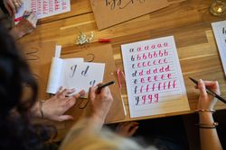 Crop faceless female students practicing lettering in classroom