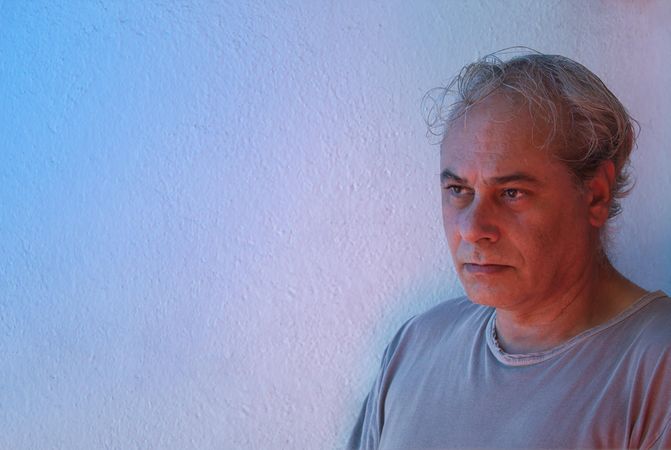 Portrait of sad middle aged man in gray shirt against light background in UV lit studio