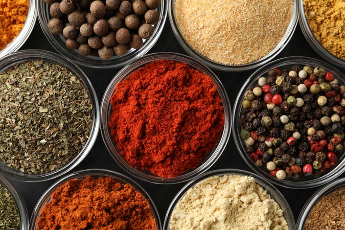 Close up top view of glass bowls full of spices on dark table