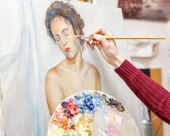 Hand of artist applying paint to female portrait