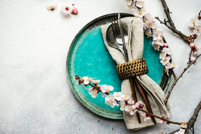 Table setting with delicate apricot blossom around elegant teal tableware on grey counter with copy space