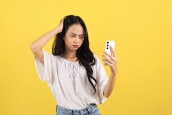 Asian Tennager Girl Wearing an White Casual Shirt, Looking Sad and Confused While Holding Smartphone