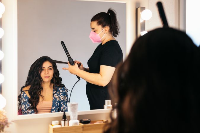 Hairdresser in a mask doing a woman's hair at a dressing table