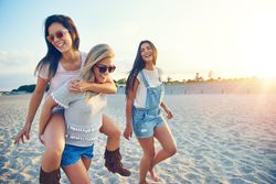 Three smiling female friends having fun walking on sand at the beach