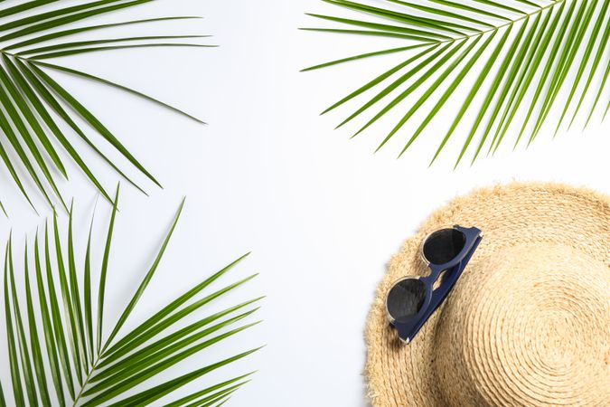 Composition with straw hat, sunglasses and palm leaves on light background. Top view, space for text