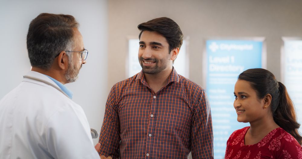 Indian Couple Visiting a Local City Hospital for a Health Check Up: Young Husband and Wife Talking to Their Doctor