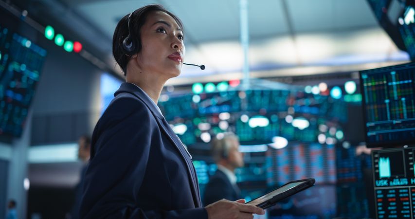 Young Asian Female Broker Working on Tablet Computer on Stock Exchange Floor.
