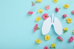 Lung cut out from paper on blue background surrounded by flowers with copy space