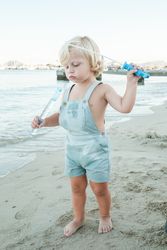 Serious curious toddler playing with soap bubble toy on beach in