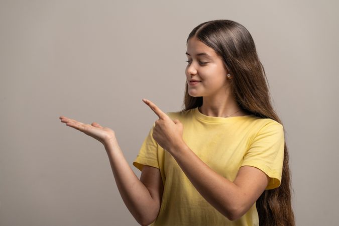 Young woman presenting something on her empty palm and pointing at it.
