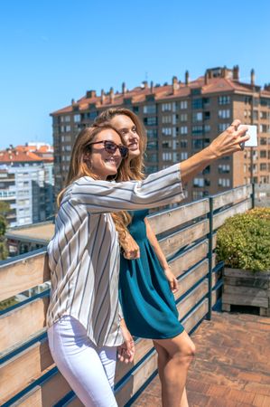 Two female friends taking a selfie in rooftop city on a summer day