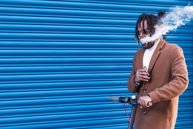 Hipster Black man with electronic cigarette on electric scooter