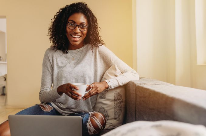Businesswoman sitting on sofa at home and working on laptop holding a mug