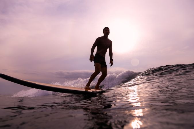Man on surf board on waving water at sunset