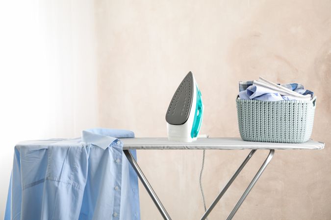 Iron and basket with clear laundry against light background, space for text