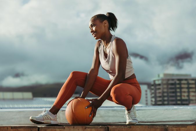 Beautiful happy woman with basketball sitting on rooftop