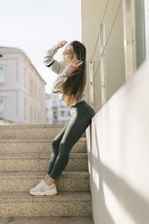 Woman leaning on wall near outdoor concrete stairs in workout clothes
