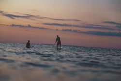 Men with paddle on surf board between waving water at sunset