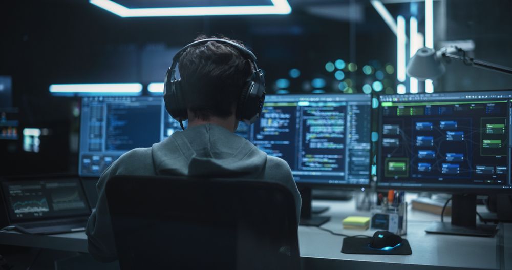 System Administrator Working in a Dark Research Facility on a Computer with Multiple Displays