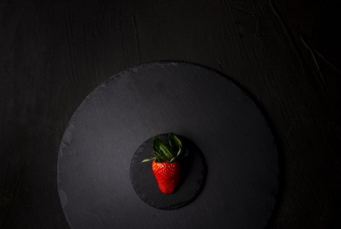 Single strawberry on a dark granite plate