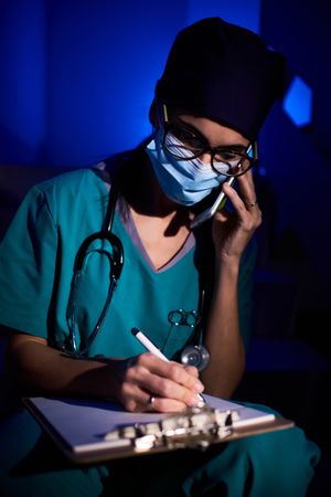 Female doctor writing medical report while talking on cellphone