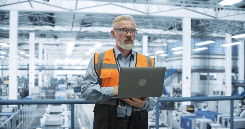 Portrait of a Thoughtful Engineer Monitoring and Analyzing Conditions at a Modern Electronics Factory with Automated Robots Working with the Help of Artificial Intelligence Software