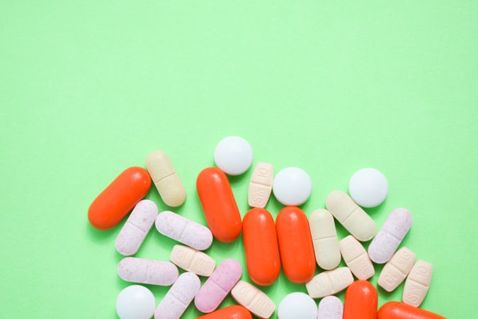 Top view of variety of pills and vitamins on green table with copy space