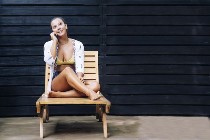 Delighted woman talking on phone while resting on deck chair