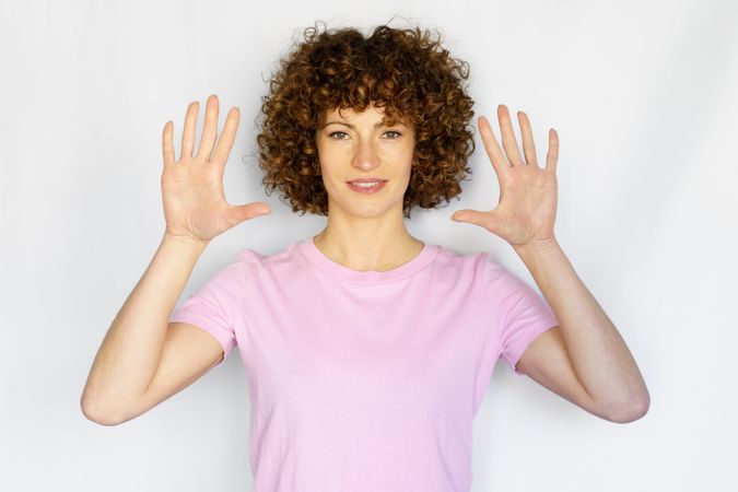 Female in light pink t-shirt standing with hands up in blank space