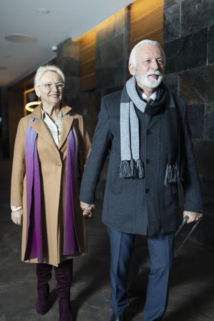 Smiling mature couple wearing scarfs and coats walking hand in hand in corridor
