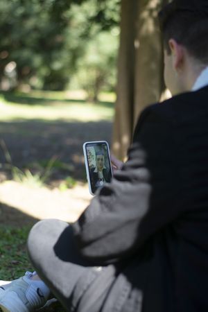 Back view of a young male student sitting on campus while using a mobile phone