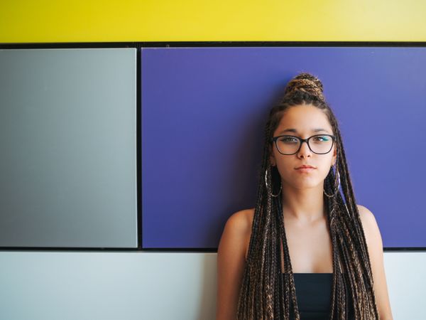 Charming teenage girl with braids in sunglasses nearby colorful wall