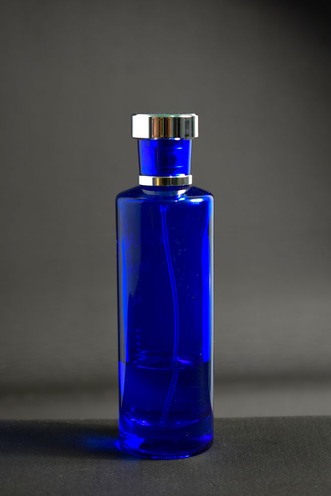 Blue perfume bottle in grey studio with copy space