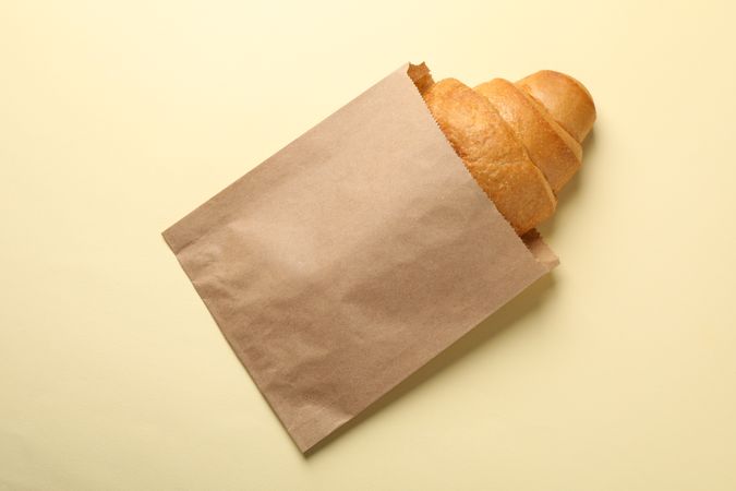 Craft paper bag with croissant on beige background, copy space
