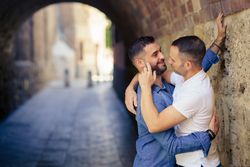 Two men facing each other about to kiss under a city bridge