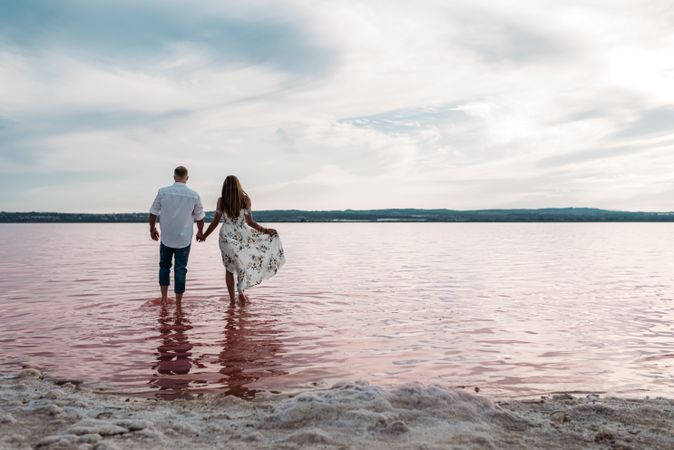 back view of adorable couple walking into an amazing beach with pink water